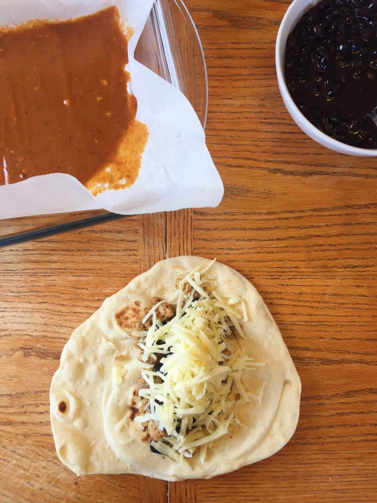 Tortilla topped with ground turkey and cheese on a table.