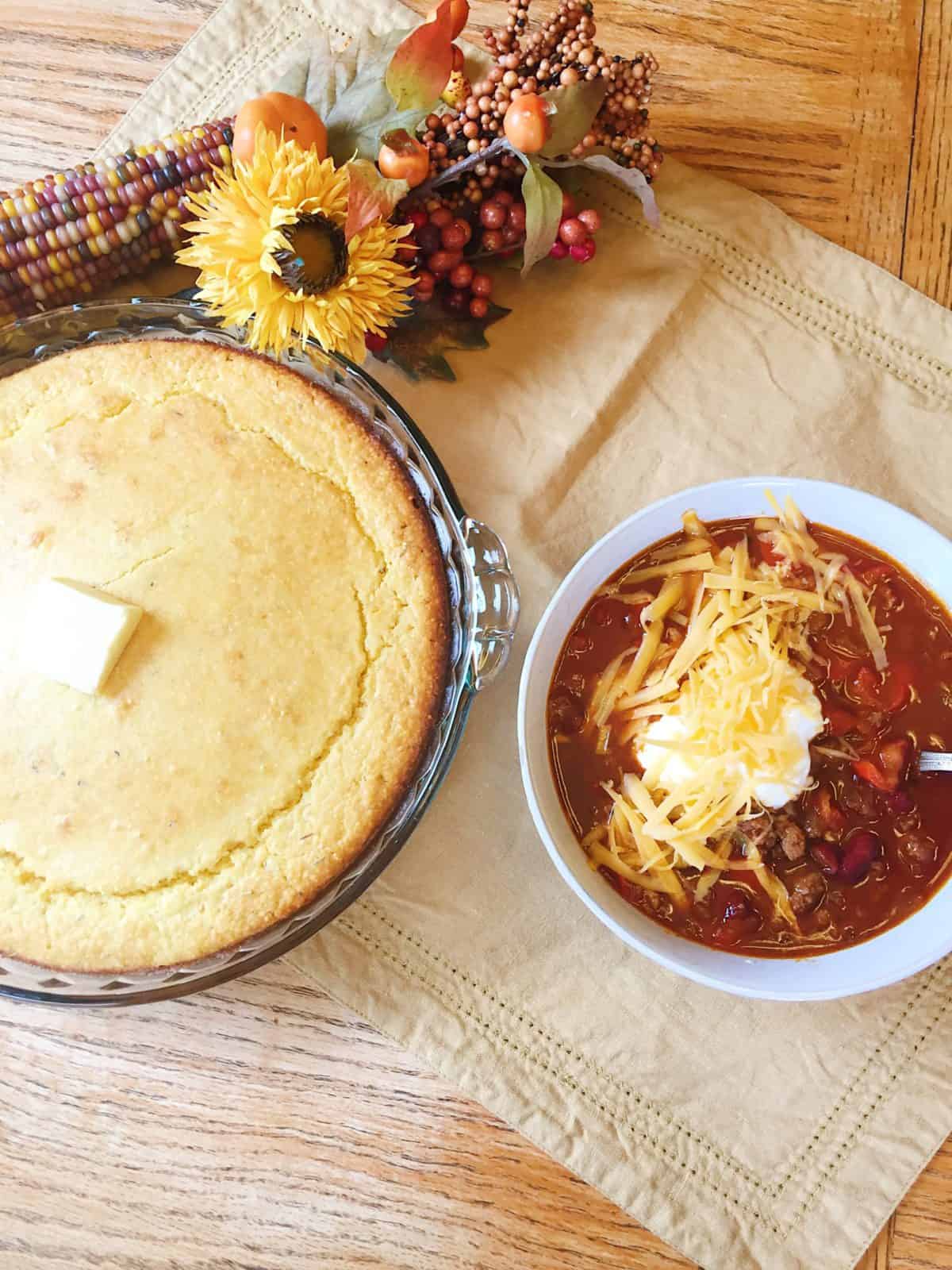 Baked cornbread in a baking dish next to a bowl of chili.