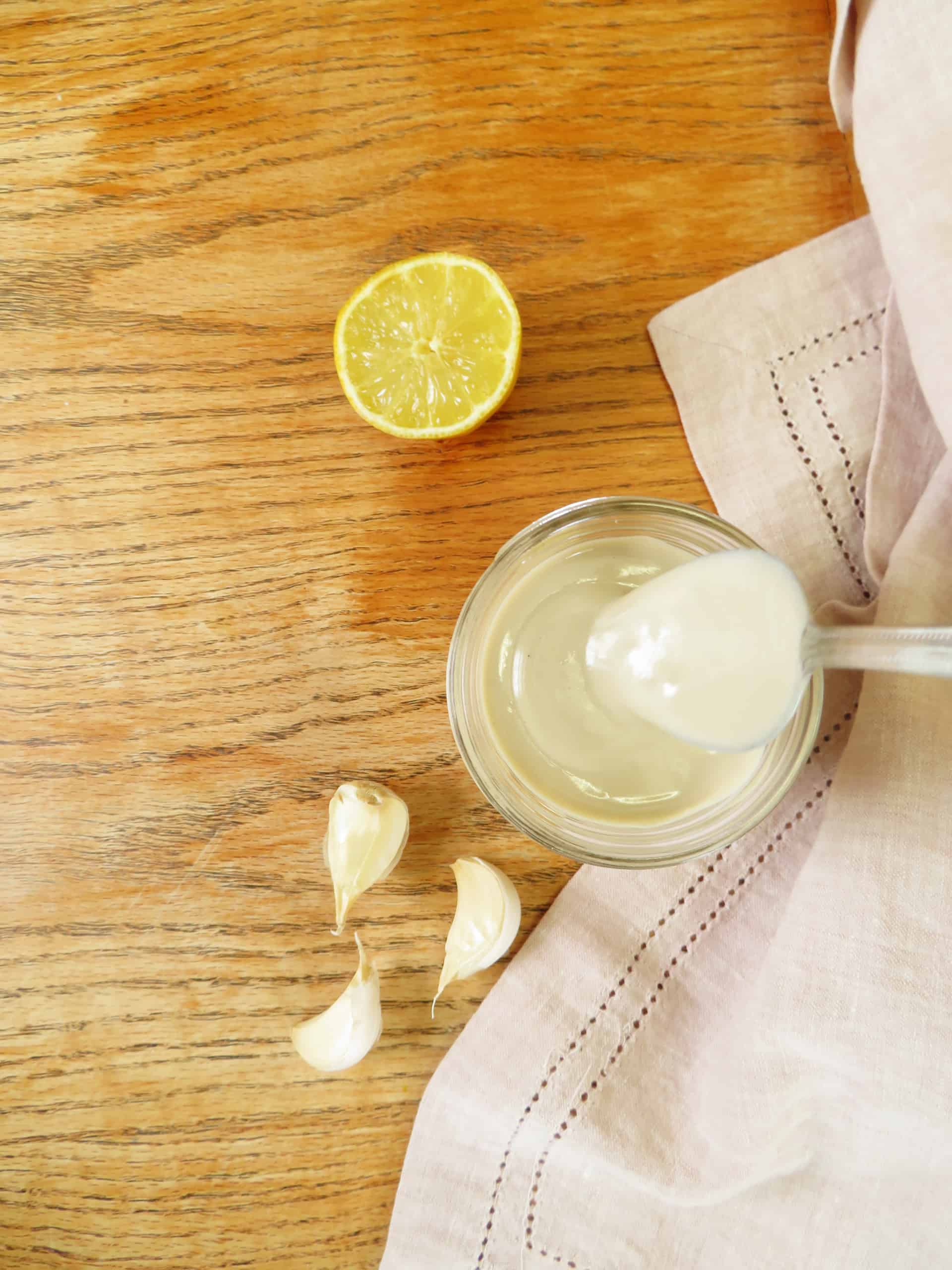 easy tahini sauce in a mason jar with garlic cloves and lemon on a table. 