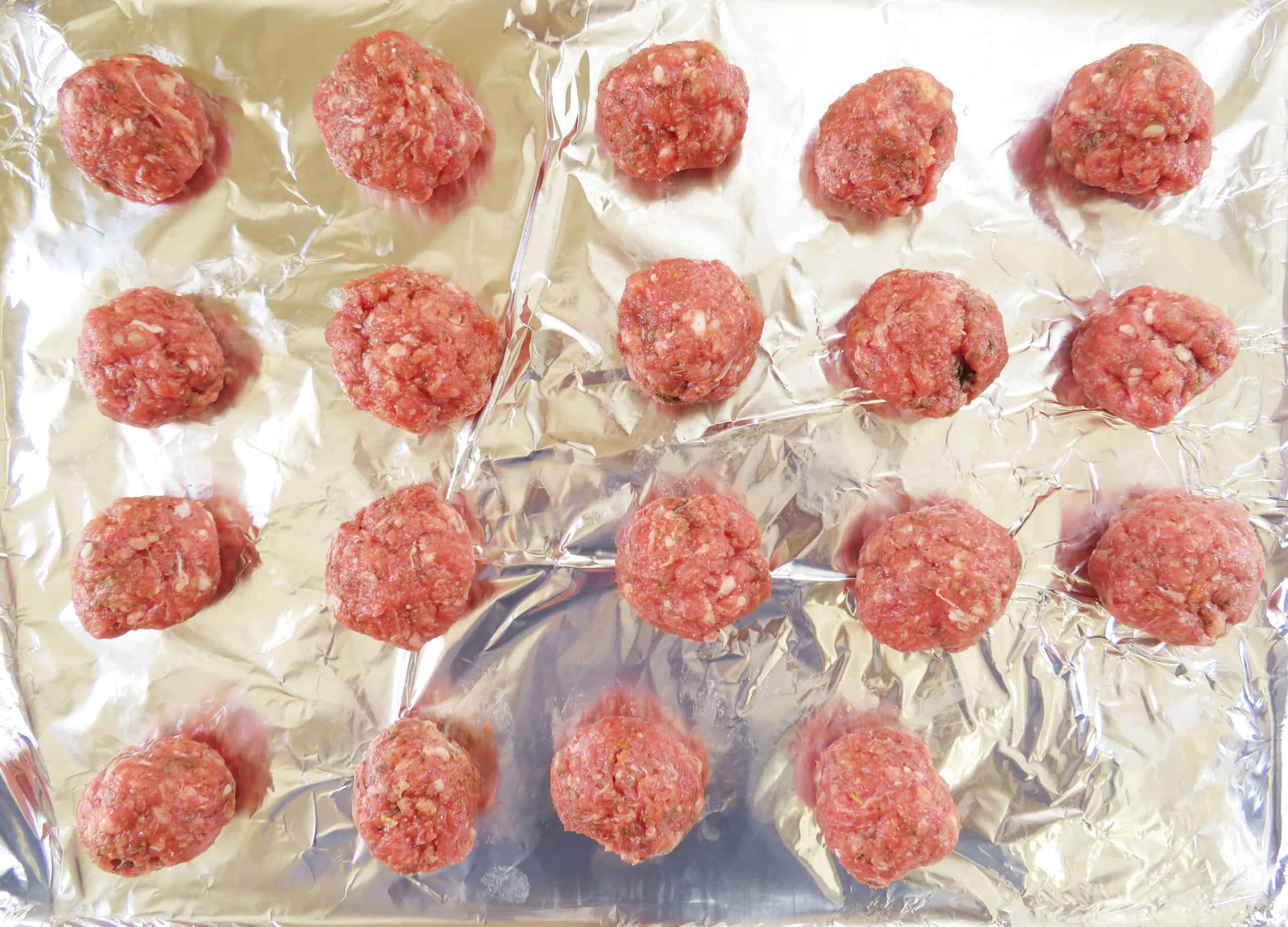Raw meatballs on a sheet pan lined with aluminum foil.