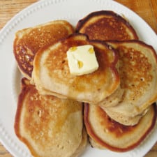 Stack of pumpkin pie spice pancakes on a plate with butter and maple syrup.
