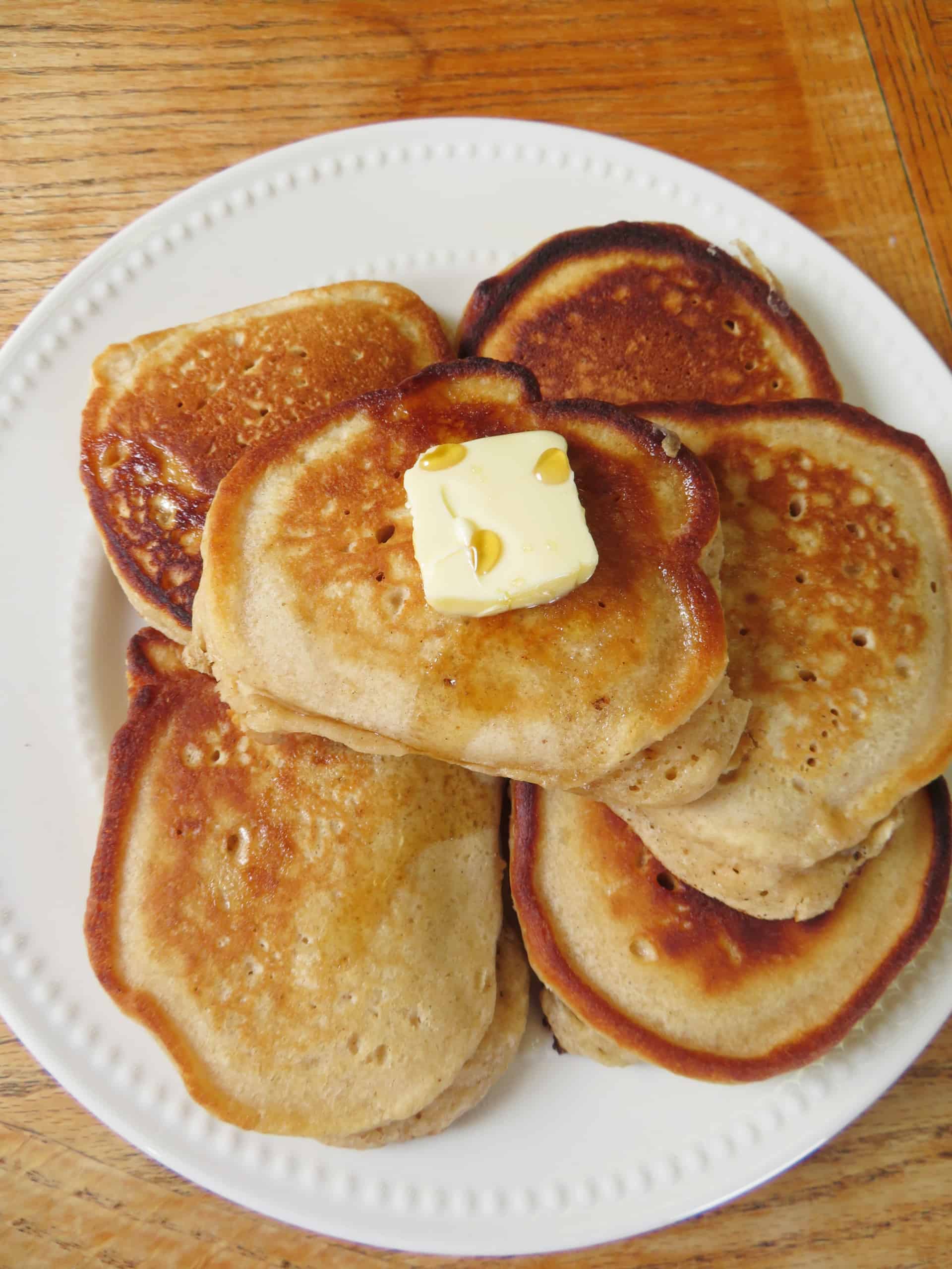 Stack of pumpkin pie spice pancakes on a plate with butter and maple syrup.