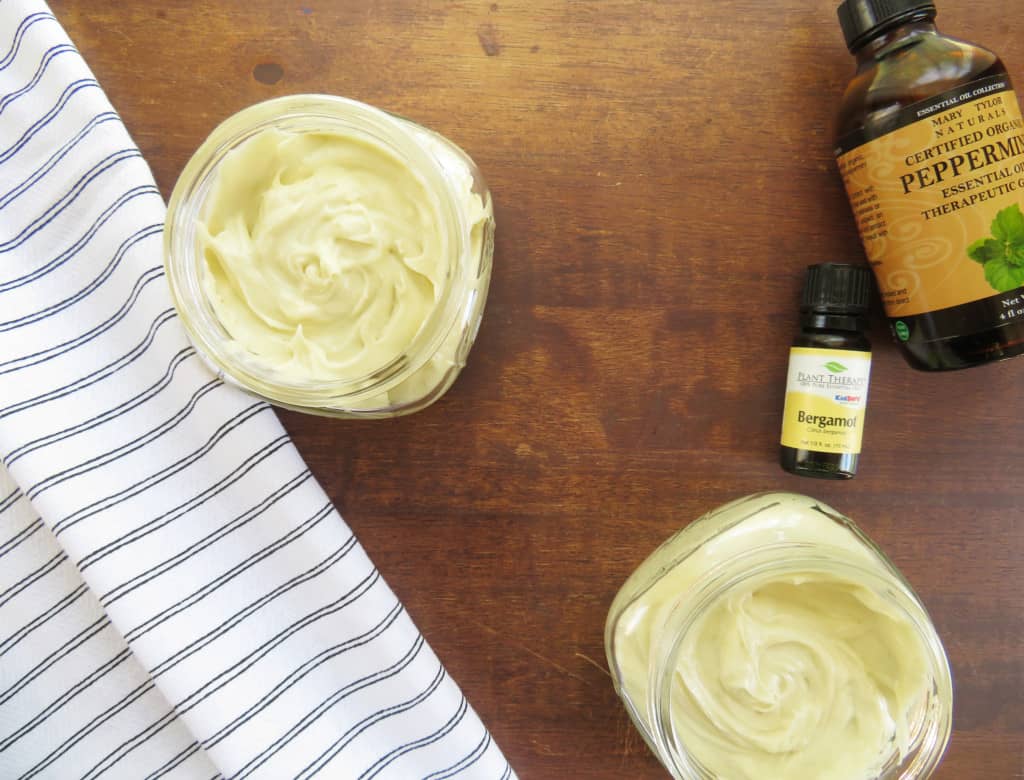 Whipped shea butter in storage containers with bottles of essential oils near by.