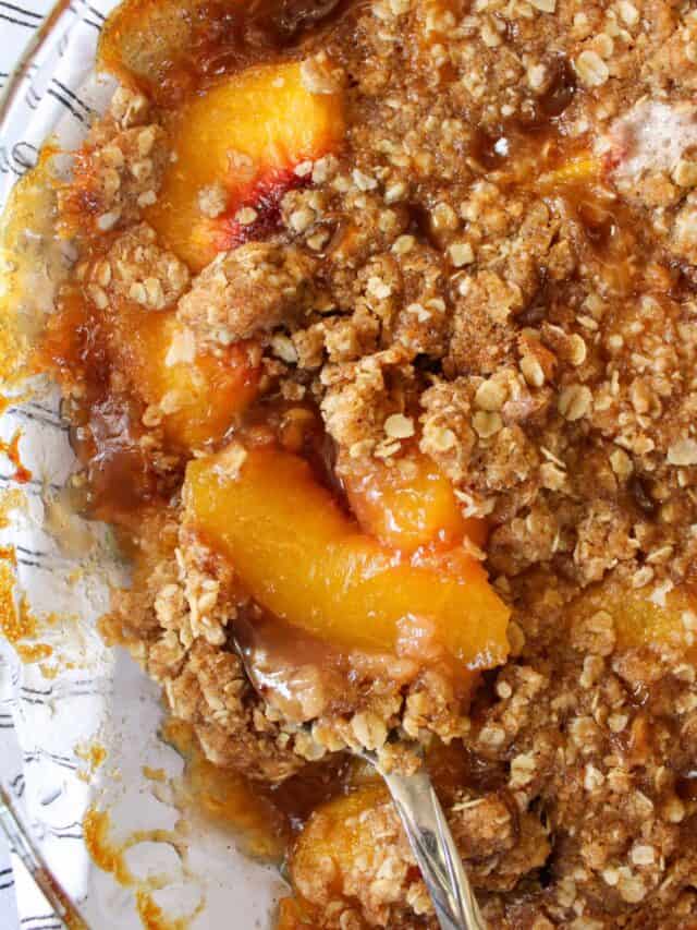 Close up on peach crisp in a pie dish with a spoon.