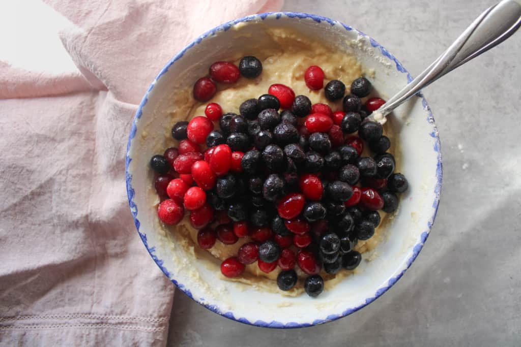 top view of berries on top of blueberry muffins batter in a bowl