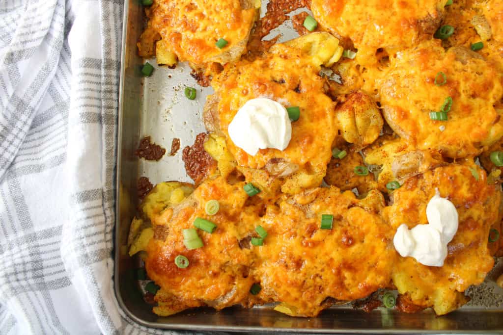 overhead of smashed yukon gold potatoes with shredded cheese, green onions, and sour cream.