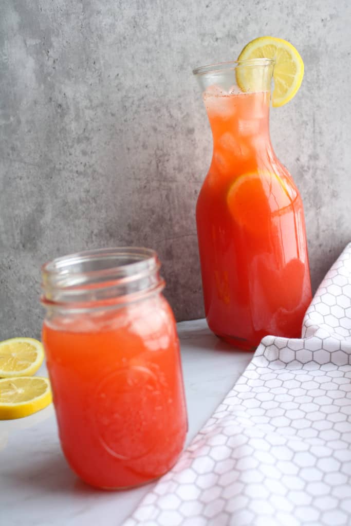 side view of a vase of strawberry lemonade with a lemon slice on the rim