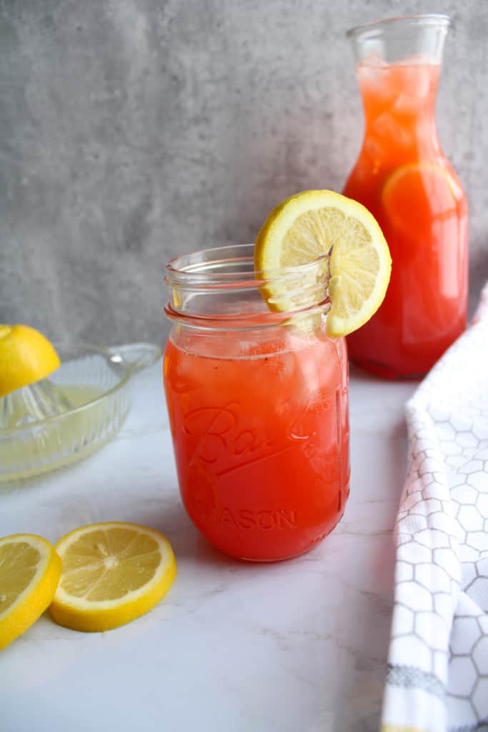 side view of strawberry lemonade in a mason jar with a lemon slice on the rim