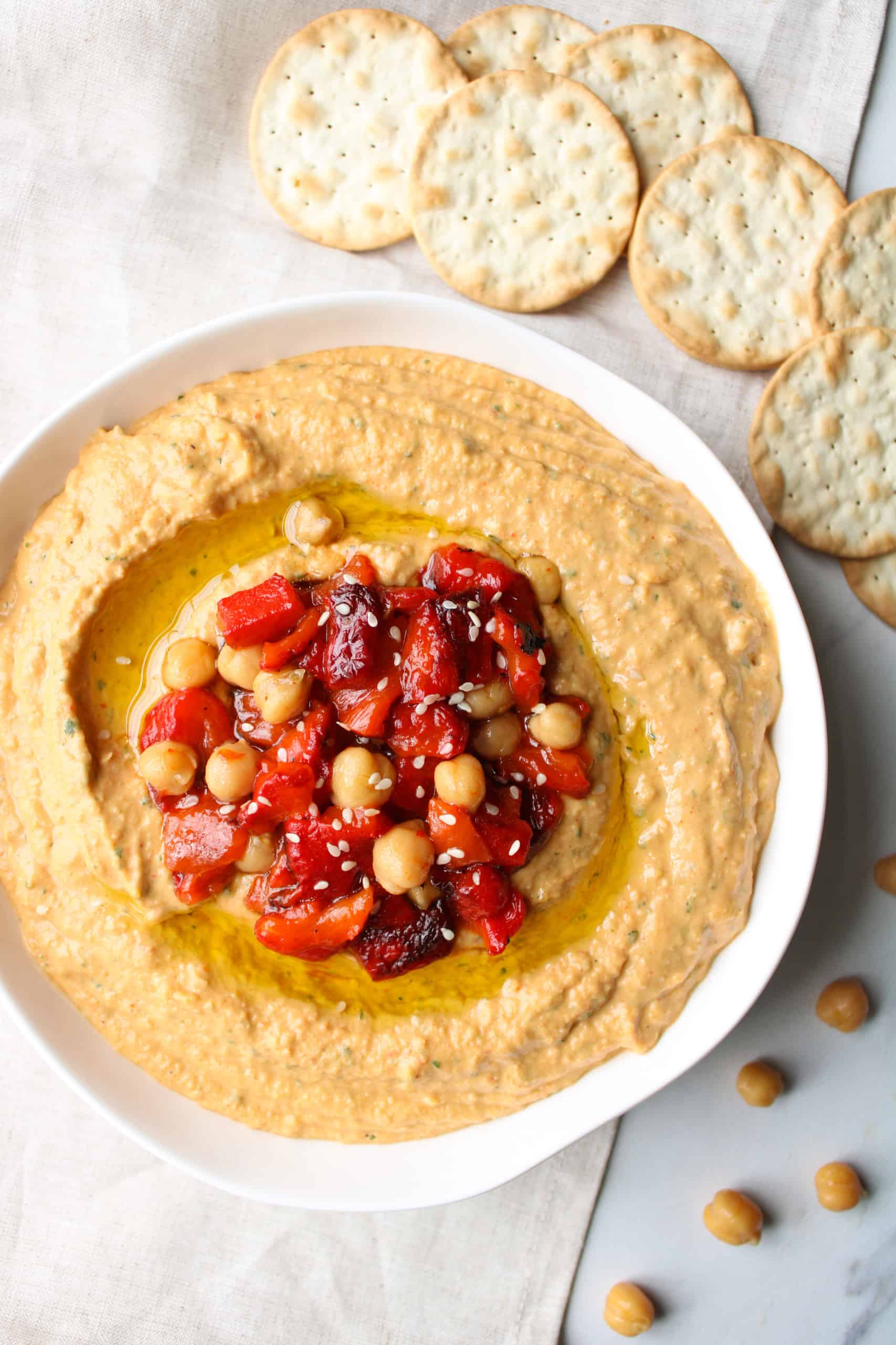 Red bell pepper hummus in a bowl with crackers on a table.