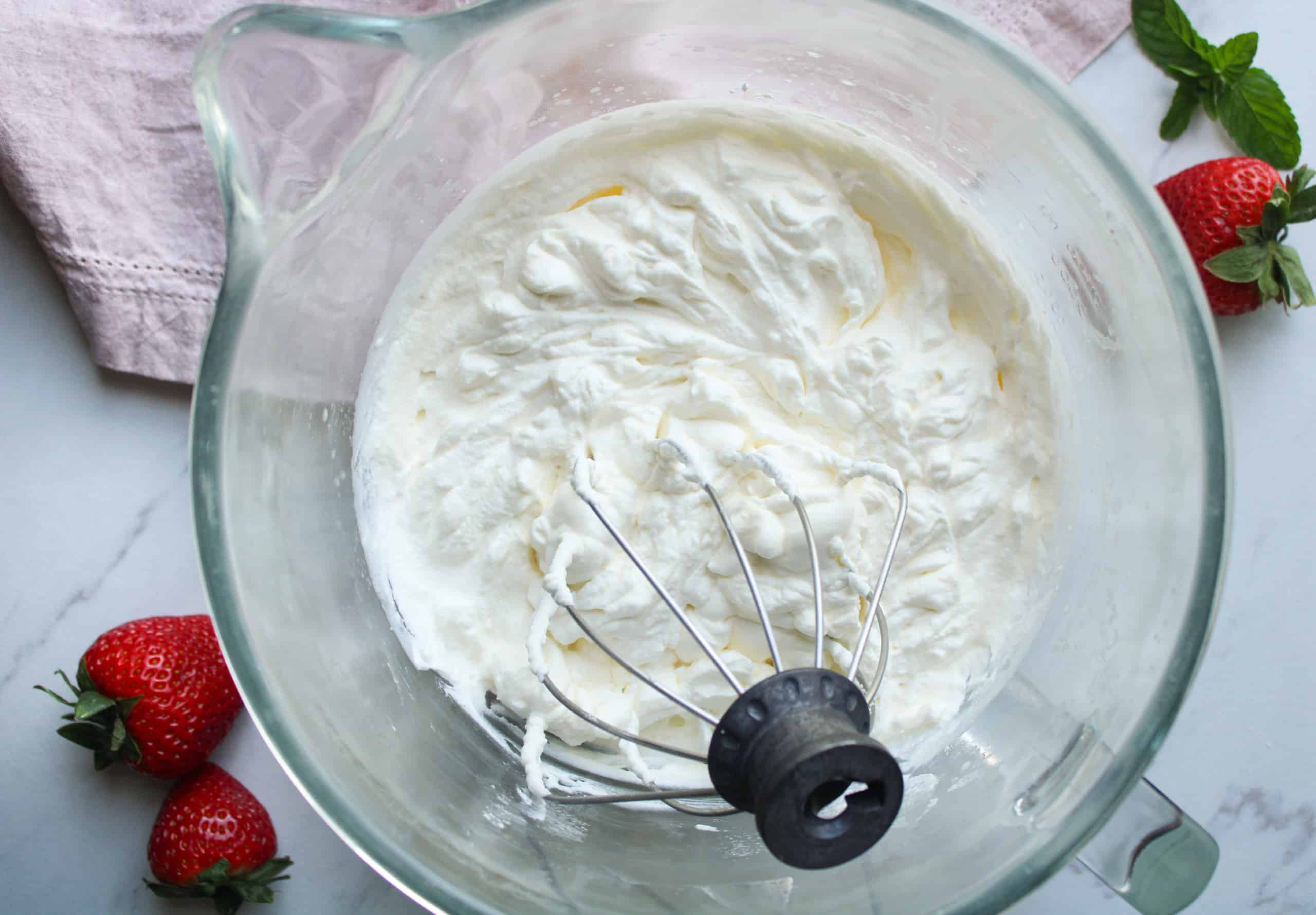 Whipped cream in a mixing bowl with fresh berries on the counter.
