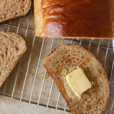 Close up of a slice of honey whole bread with butter and honey on a wire rack.