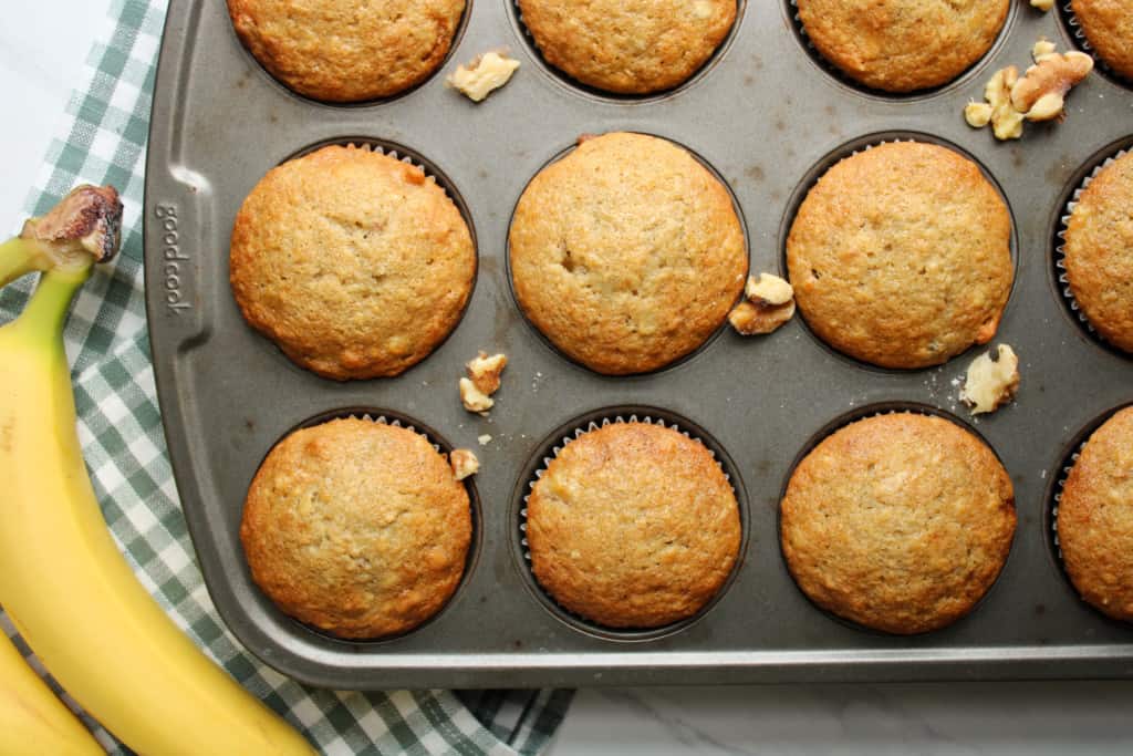 Baked banana nut muffins in a muffin pan with a banana. 