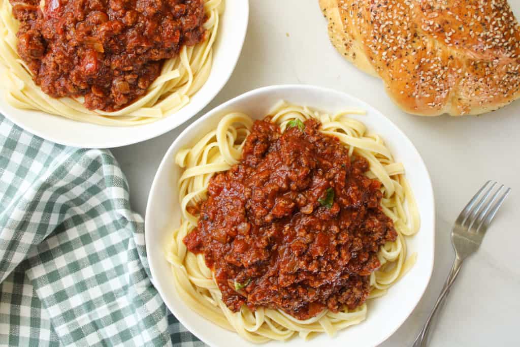 Bison meat sauce over pasta in a bowl on a table with bread. 