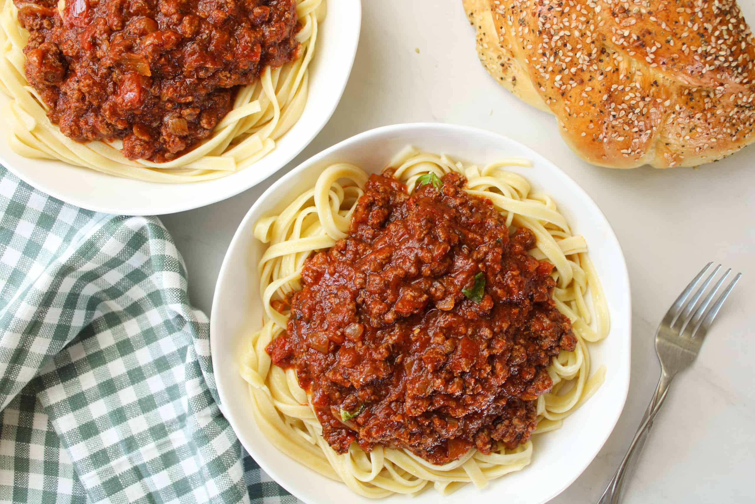 Bison meat sauce over pasta in a bowl on a table with bread.