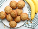 Overhead view of banana muffins on a plate with a bunch of bananas.