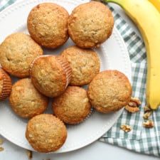 Overhead view of banana muffins on a plate with a bunch of bananas.