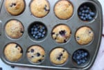 Overhead of lemon blueberry muffins in a muffin pan with fresh blueberries.
