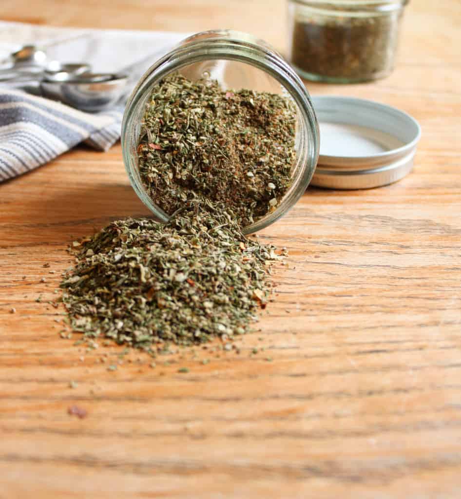 Close up of savory no sugar sausage spices spilling out of jar onto table. 