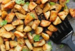 Close up on crispy potatoes with za'atar seasoning in a baking dish with a spatula.