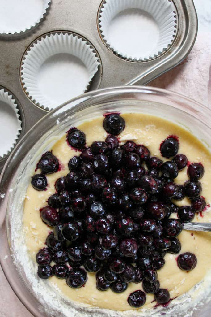 Close up on muffin batter with blueberries on top in a bowl. 