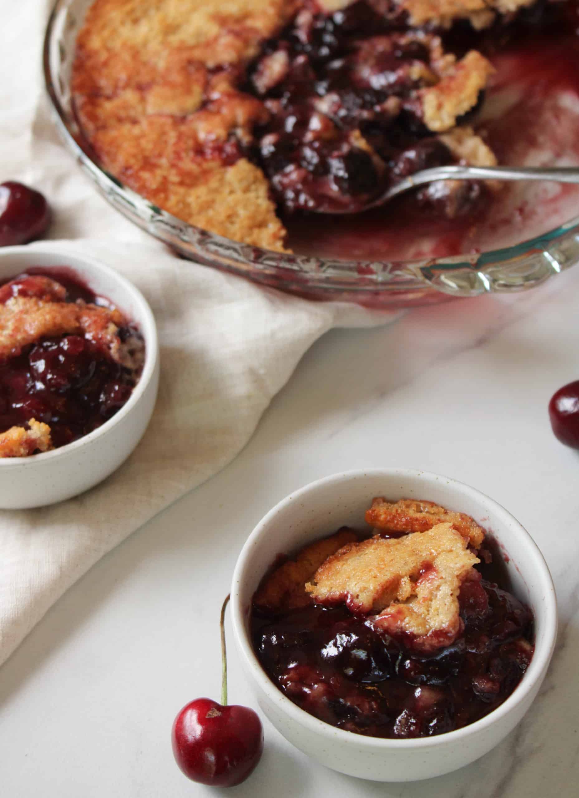 Cherry cobbler in bowls with fresh cherries on a counter.