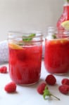 Raspberry lemonade in a mason jar with fresh raspberries on a table.