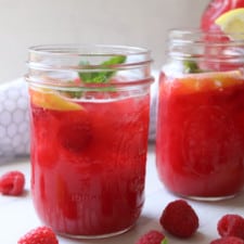 Raspberry lemonade in a mason jar with fresh raspberries on a table.