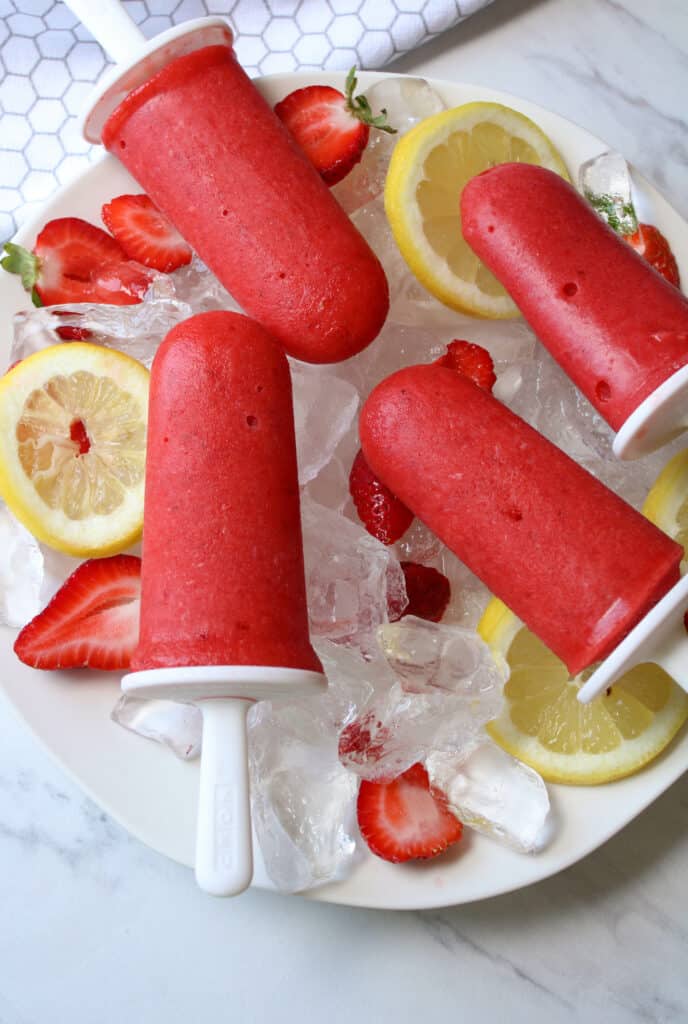 Plate of strawberry lemonade popsicles over ice and fresh fruit. 