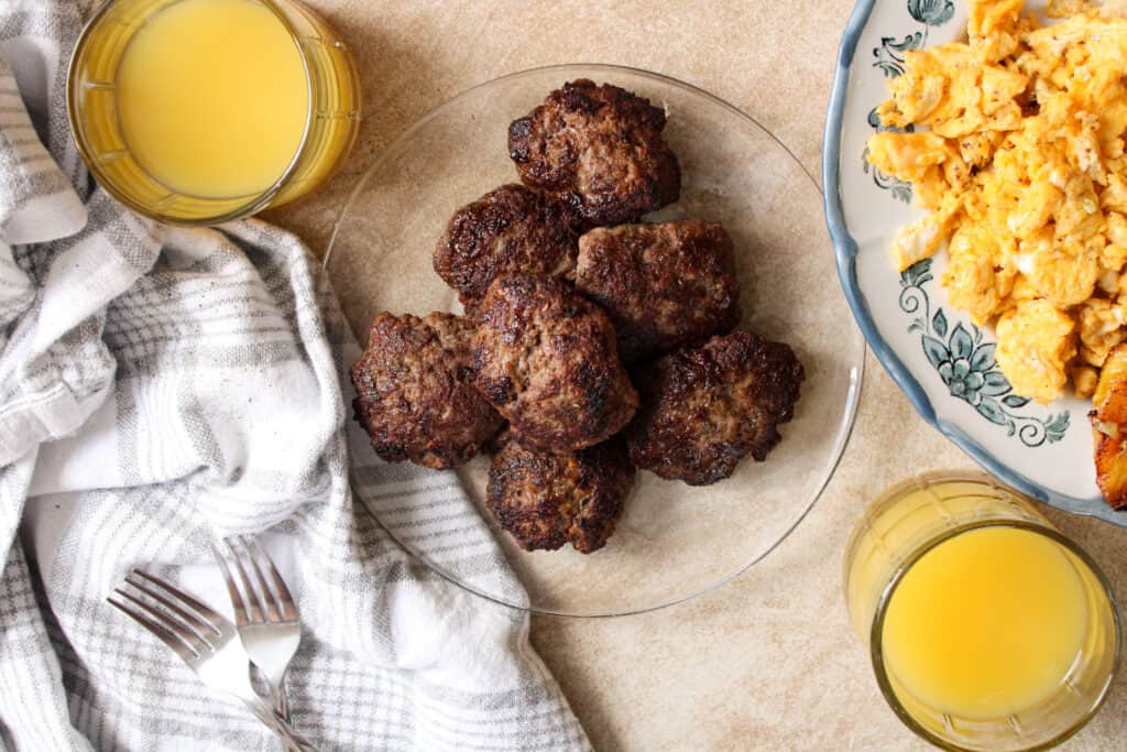 Beef breakfast sausage patties on a plate with scrambled eggs and orange juice. 