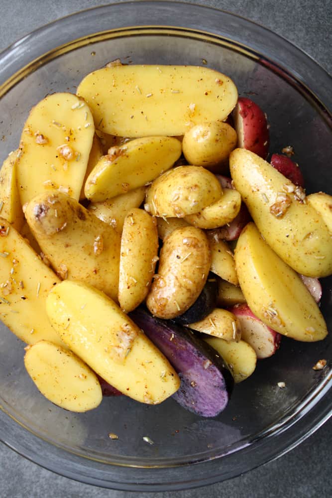 Close up on sliced potatoes with garlic and rosemary in a bowl. 