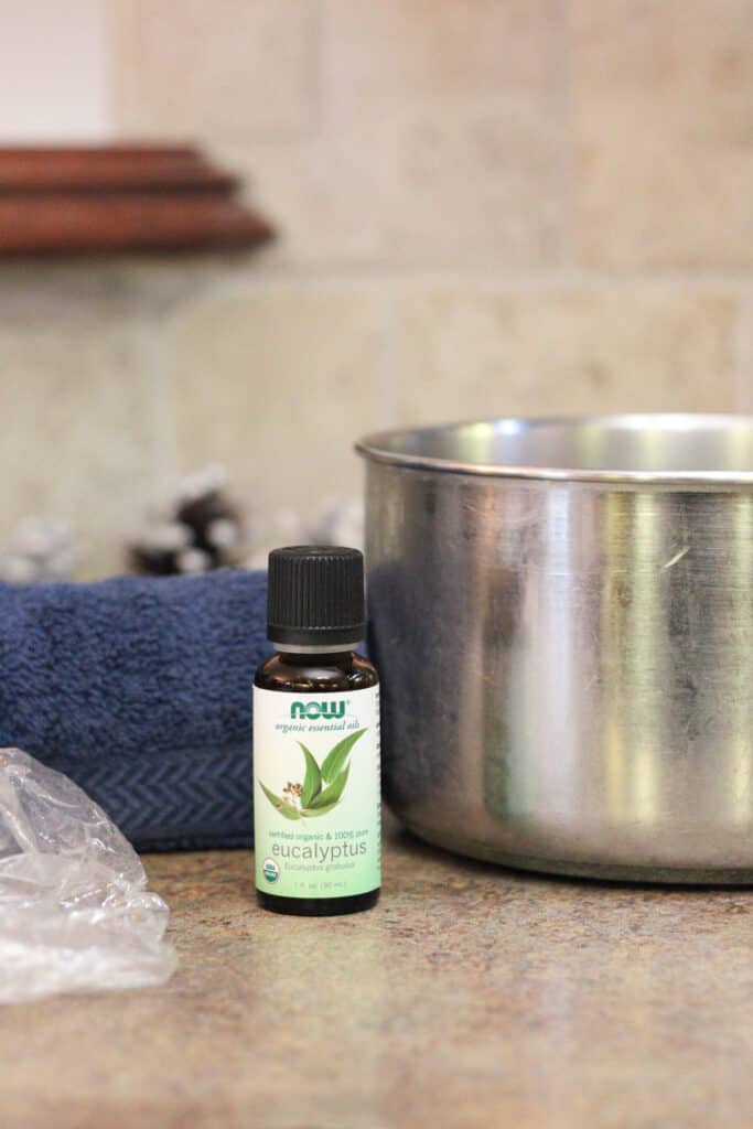 Side view of essential oil bottle with towel and pot on a table. 