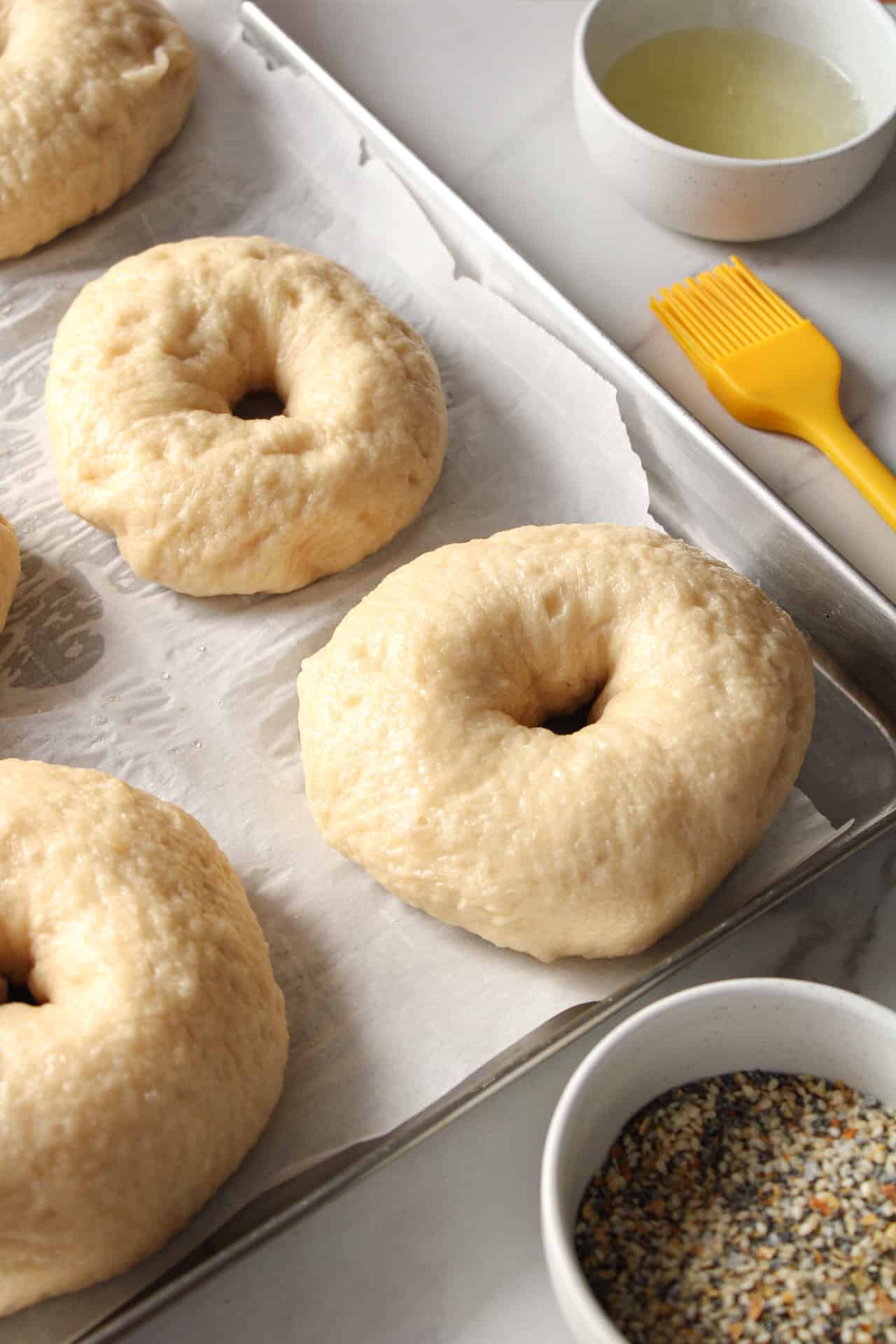 Boiled bagel brushed with an egg wash on a sheet pan.