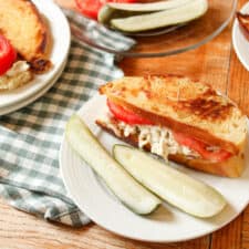 3/4 view of a chicken sandwich on a plate with two pickles.