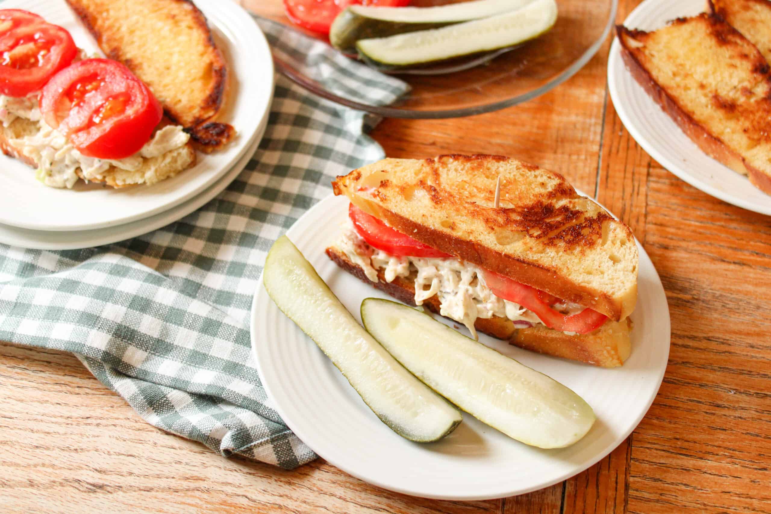 3/4 view of a chicken sandwich on a plate with two pickles.