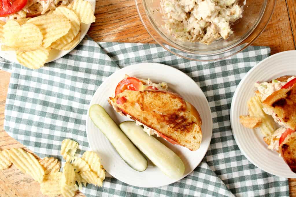 Overhead view of chicken salad sandwich on a plate with pickles and chips.