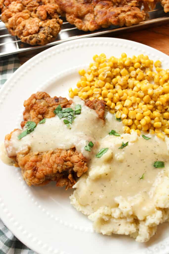 Close up on chicken fried steak, gravy, mashed potatoes, and corn on a plate.