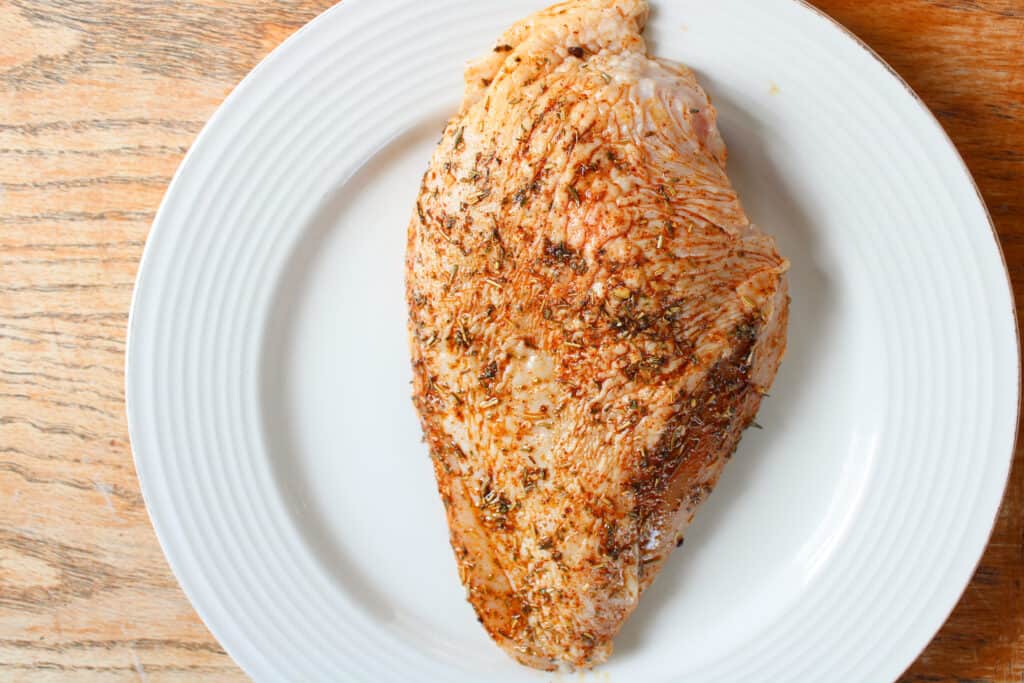 Raw seasoned chicken breast on a plate.