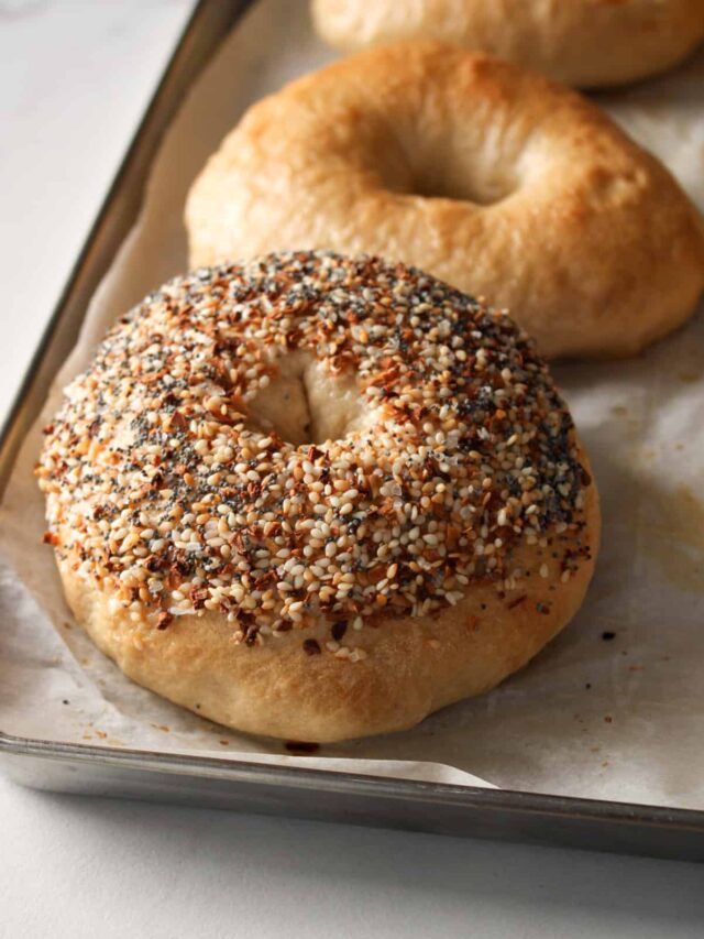 Close up on an everything bagel on a sheet pan.