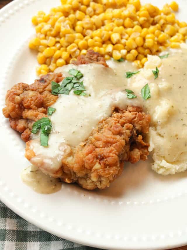 texas style chicken fried steak on a plate with gravy, mashed potatoes and corn.