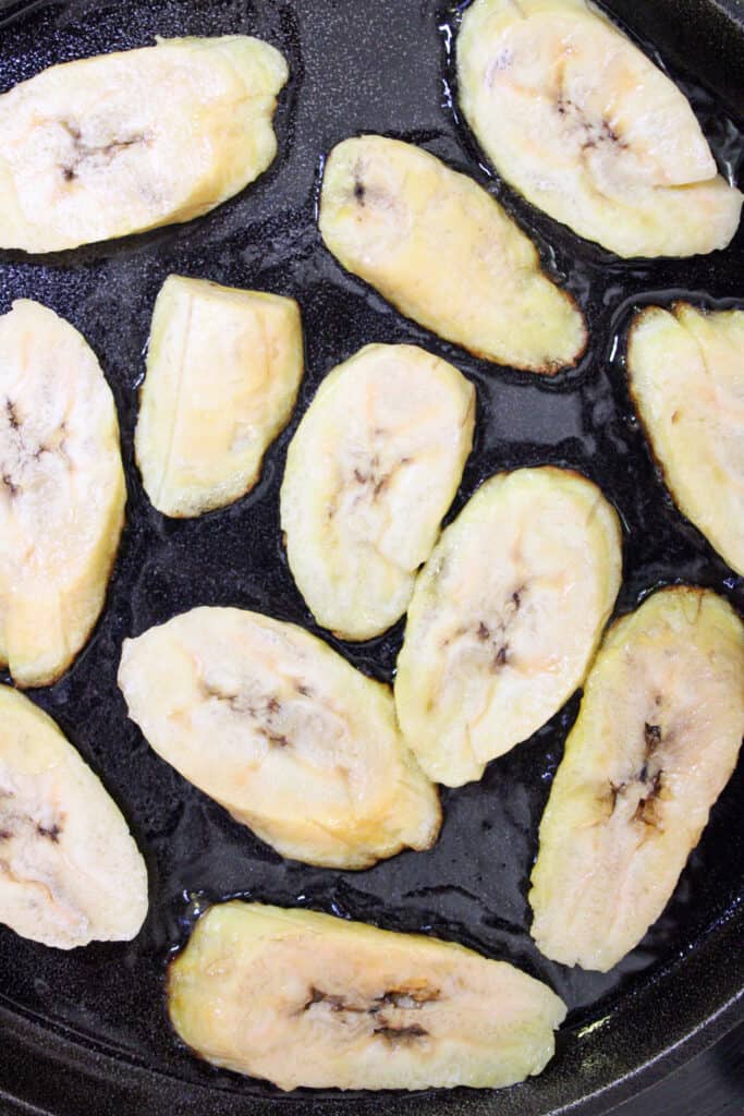 Uncooked plantains in a cast iron skillet.