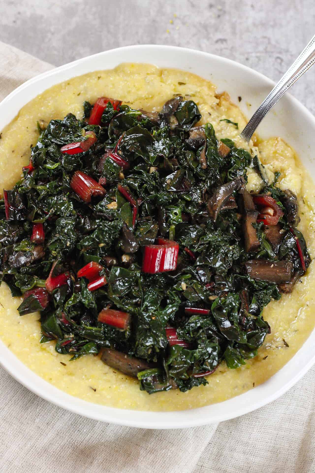 3/4 view of creamy polenta with greens and mushrooms.