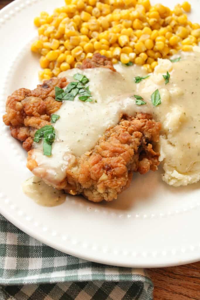 Close up side view of chicken fried steak with gravy on top on a plate.