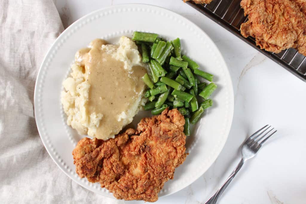 Overhead view of a plate of chicken fried chicken with green beans,  mashed potatoes and dairy free pan gravy. 