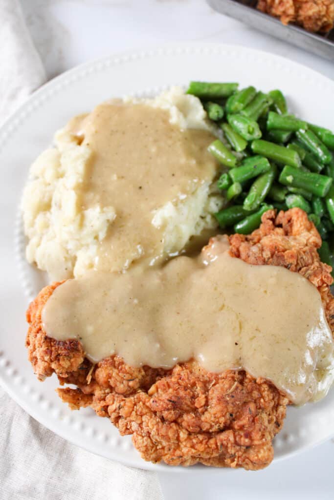 Close up on chicken fried chicken on a plate covered in homemade pan gravy. 