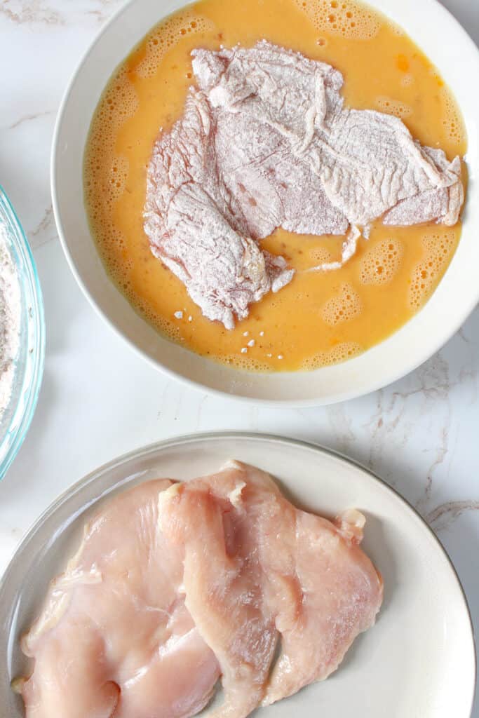 Floured chicken breast on a plate with whisked eggs.