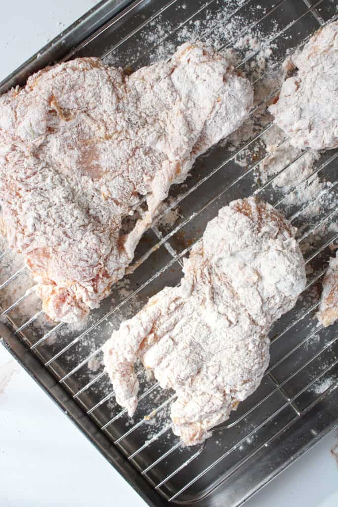 Chicken breast on a wire rack coated in egg and flour.