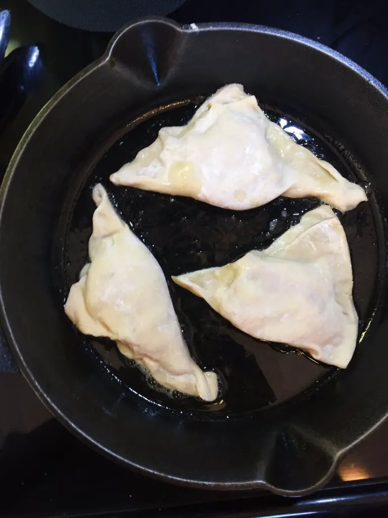 Uncooked chicken dumplings with cabbage in a skillet process image as they cook.