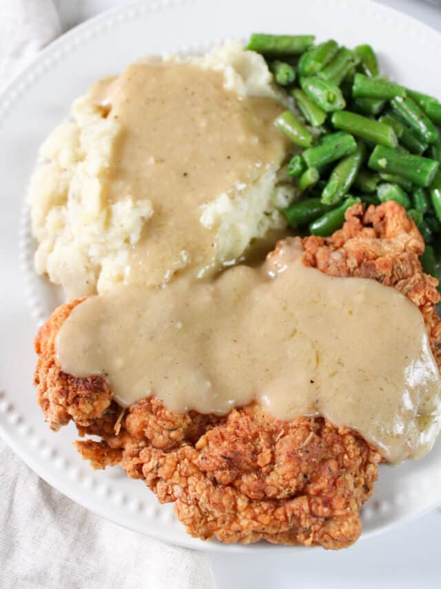 Close up on a plate of chicken fried chicken with pan gravy, mashed potatoes, and green beans.