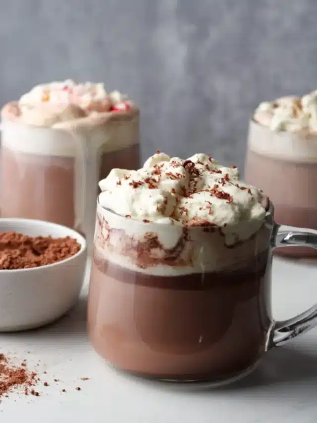 Side view of 3 mugs of hot chocolate with whipped cream.