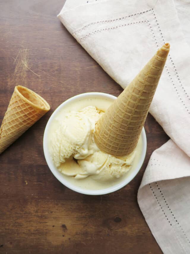 Close up on vanilla ice cream in a bowl with an ice cream cone on top.